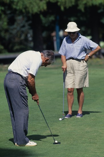 10101183 SPORT Ball Games Golf New Zealand. North Isalnd. Taupo. Middle aged couple on a putting green with man taking a putt. .