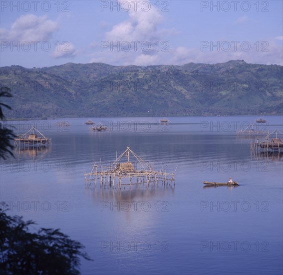 INDONESIA, Lombok, Lembar, Bamboo fishing platforms in the sea with a man in a canoe rowing towards one