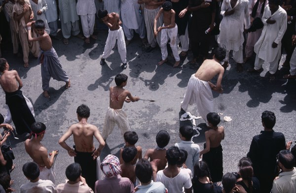 PAKISTAN, N W Frontier Province, Peshawar , "Mohurrum Shia muslim festival commemorating death of Husayn ibn Ali, grandson of Muhammad.  Boys beating themselves with chains in ceremonial mourning. "