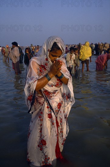 INDIA, West Bengal, Sagar Island, Woman pilgrim praying during three day Sagar bathing festival at point where the Ganges joins the sea.  Other people in water behind her.