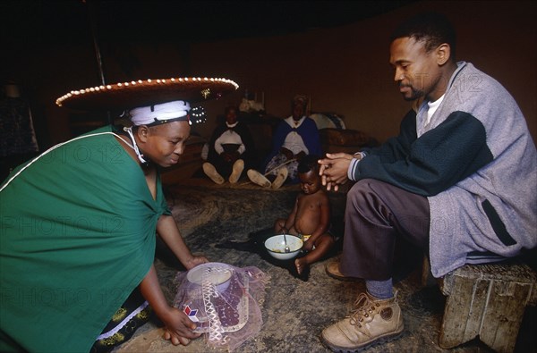 SOUTH AFRICA, Kwa Zulu Natal , Msinga, Zulu woman kneeling to give tea to her seated husband.