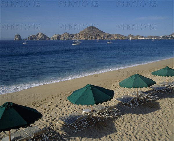 MEXICO, Baja California, Cabo San Lucas, Menano beach area View over beach to surrounding coastline Sun longers & shades in foreground