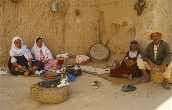 TUNISIA, Matmatah, Troglodyte Cave with men and women sitting by the wall with a cat in a basket in the foreground