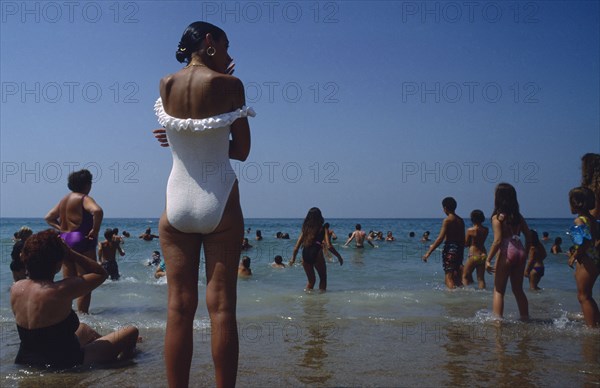 FRANCE, Aquitaine, Pyrenees Atlantiques, Biarritz.  Busy beach scene with people standing and playing in the water.