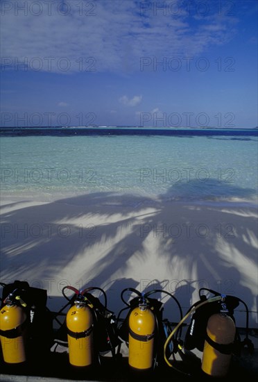 MALDIVES, Nika Island, View out to sea with scuba diving tanks on the beach in the shadow of coconut palm trees