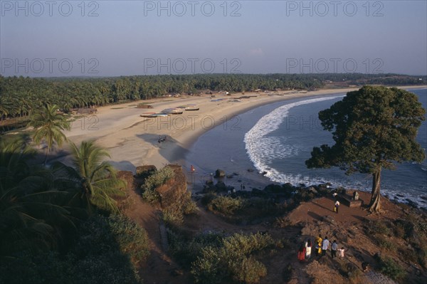 INDIA, Kerala, Bekal, View along the beach and coastline with people standing by tree on rocky promontory in the foreground