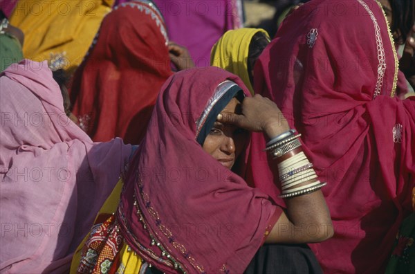 INDIA, Rajasthan, Rajasthani woman looking over her shoulder amongst crowd wearing colourful saris.