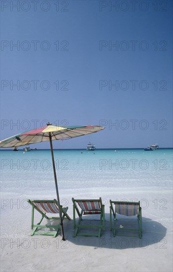 THAILAND, Pattaya , Coral Island, Empty sun loungers and umbrella on beach with boats moored just off shore