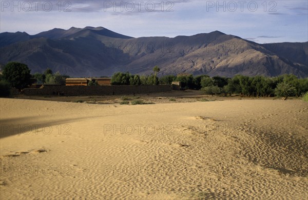CHINA , Tibet  , Samye, Wind rippled encroaching sand with mountain backdrop.