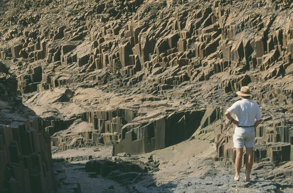 NAMIBIA, Landscape, Desert, Organ Pipes.Outcrop of volcanic basalt rock in desert . Man standing near rocks