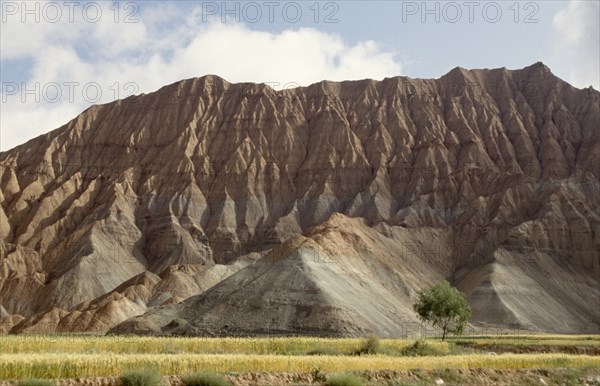CHINA, Qinghai, View of soft eroded rocks above a wheat field in a remote valley near the Yellow River.