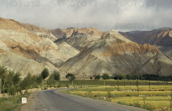 CHINA, Qinghai  , Near Yellow River , "Eroded rocks above wheat field, high altitude remote valley with road in the foreground"