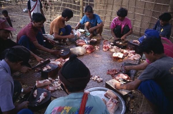 THAILAND, North, Mae Sariang, Mae Lui Village. Group of Karen refugees in a circle butchering a pig