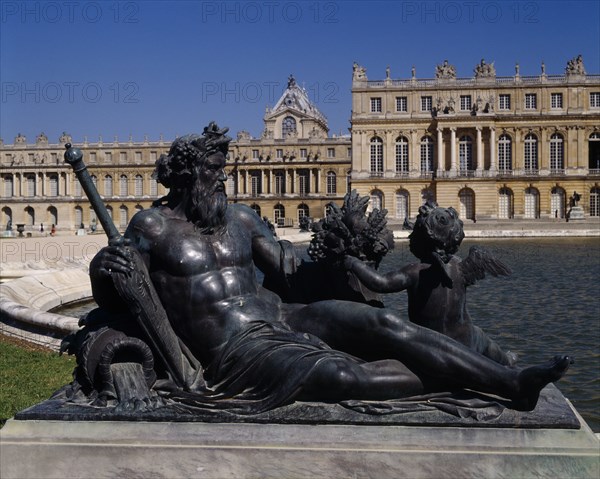 FRANCE, Ile de France, Yvelines, Versailles . Part view of palace behind bronze reclined statue of man with child next to pond