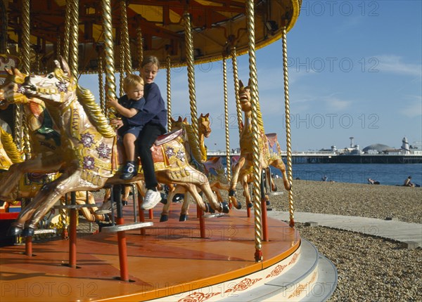 ENGLAND, East Sussex, Brighton, Young girl & boy on carousel Seafront .