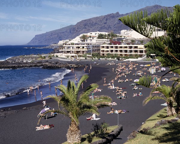SPAIN, Canary Islands, Tenerife, Playa de la Arena near Los Gigantes with sunbathers on black sandy beach and apartments in the distance