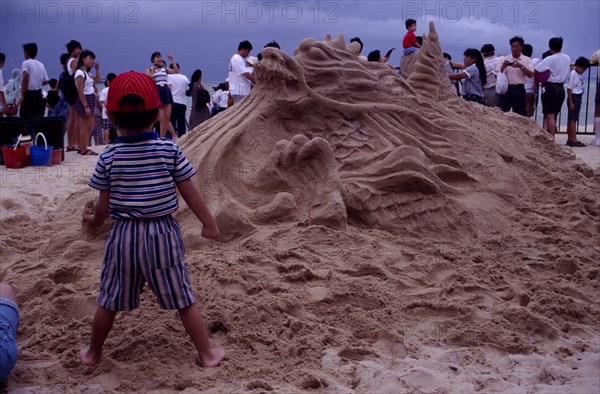 SINGAPORE, Beach, Sand sculpture of a Dragon with a boy standing in front of it holding a handful of sand