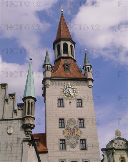 GERMANY, Bavaria, Munich, Clock tower with ornate clock and coat of arms with parts of the rooves of other buildings visible