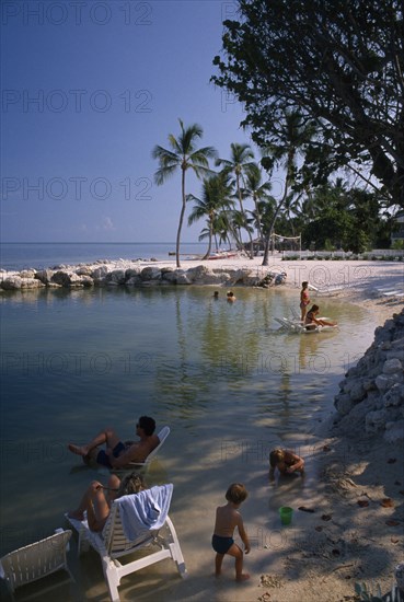 USA, Florida, Islamorada, "Cheech Lodge Beach with palms, people sitting on sun loungers in the water and children playing in the foreground"