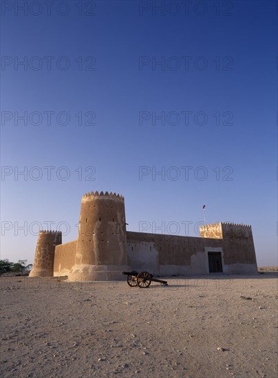 QATAR, Zubara, "Exterior view of a fort with crenellated towers, built in 1938 and used as a police border post, now a museum.  A cannon in the foreground.   "
