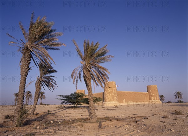 QATAR, Zubara, "Exterior view of a fort with crenellated towers, built in 1938 and used as a police border post, now a museum.  Palm trees in the foreground."