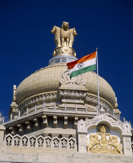 INDIA, Karnataka, Bangalore, "Vidhana Soudha building.  Exterior detail of roof dome, crest, flag and gold statue on top.  Built in 1954 housing the Secretariat and the State Legislature. "