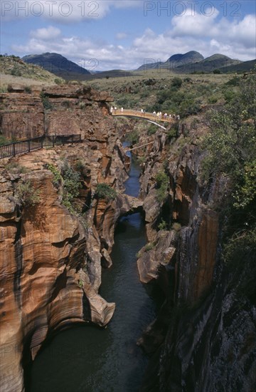 SOUTH AFRICA, East Transvaal, Blydes River Canyon, Bourkes Luck Potholes with people crossing bridge over narrow water filled canyon and mountains in the distance