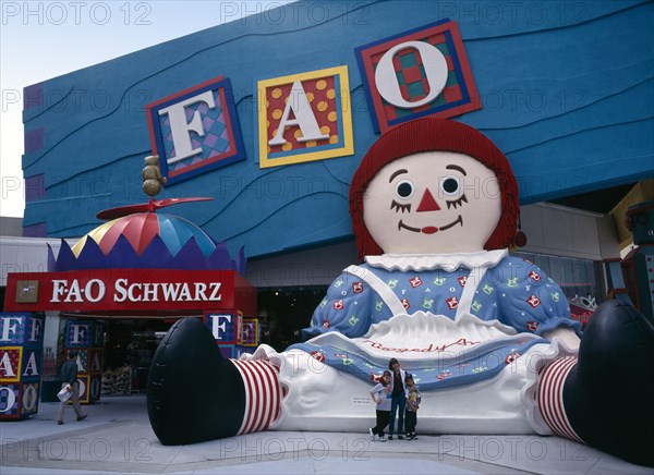 USA, Florida, Orlando , International Drive. Pointe Orlando Shopping Area. FAO Schwartz Toy store chain exterior with a family having their photograph taken next to a giant Raggedy Ann statue