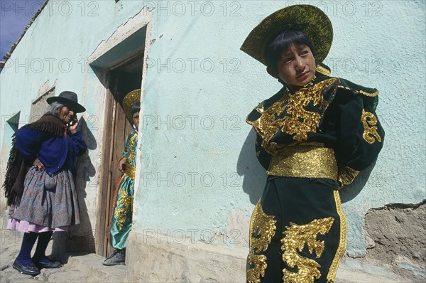 BOLIVIA, Potosi, Boy in costume in front of light green house with old woman standing by doorway talking to another boy in costume inside the house