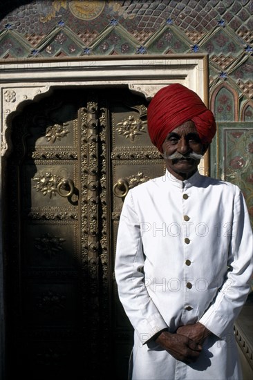 INDIA, Rajasthan, Jaipur, Palace guard dressed in white and wearing a red turban standing by ornate doorway