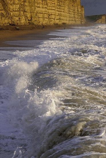 ENGLAND, Dorset, West Bay, Chesil Bank with waves breaking on the pebble beach below the cliffs