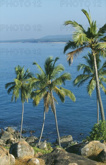 INDIA, Kerala, Kovalam , Coastal scene with men standing on rocks at the seas edge