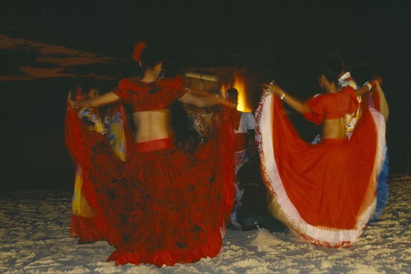 MAURITIUS, Sega Dancers, Women in red costume dancing on the beach at night.  Sega is the national dance and musical form of Mauritius.