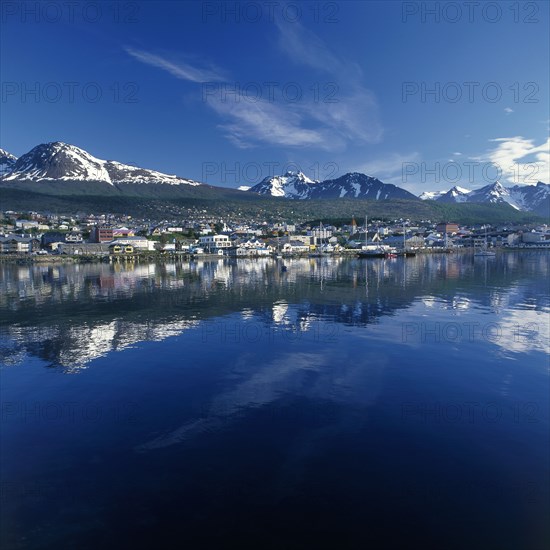 ARGENTINA, Tierra del Fuego, Ushuaia, The town of Bahia Ushuaia reflected in still water with distant snow capped mountains in a typical Patagonian landscape