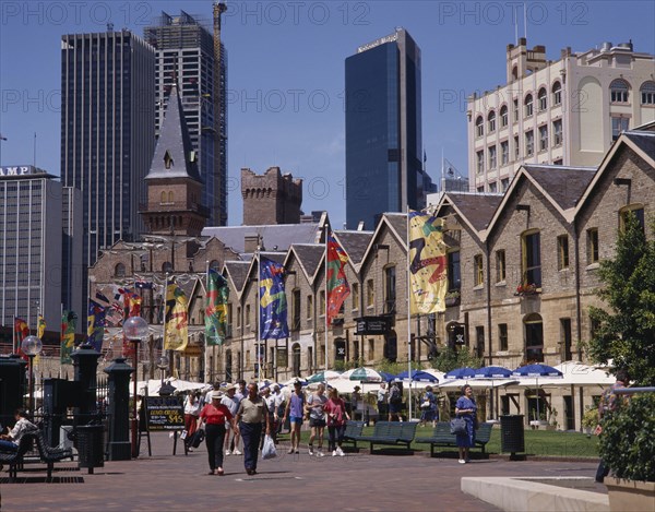 AUSTRALIA, New South Wales, Sydney, The Rocks harbourside area with people walking past restaurants festooned with umbrellas and flags