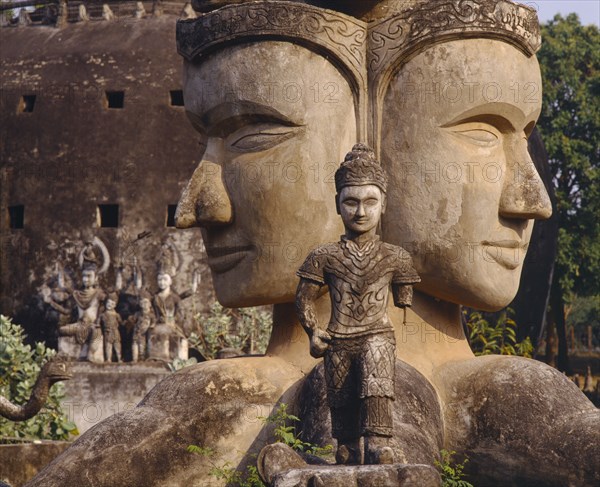 LAOS, Vientiane, Wat Xieng Khwan or the Buddha Park.  Giant twin heads with small statue in the foreground.