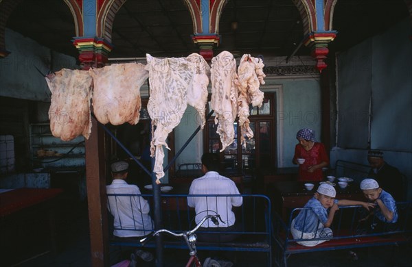 CHINA, Xinjiang, Kashgar, Carcasses of fat hanging outside a restaurant with people sitting at tables