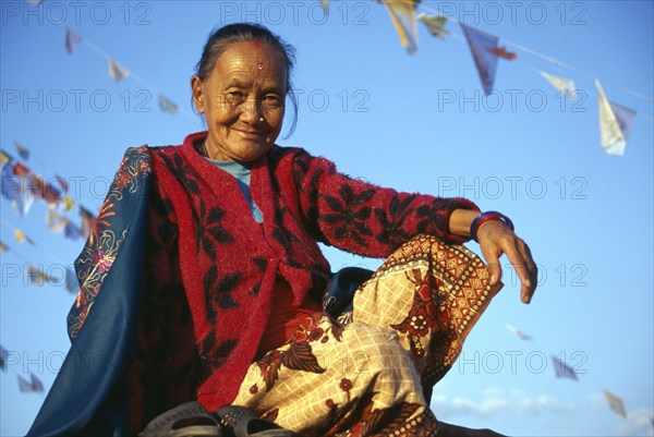 NEPAL , Kathmandu, Bodnath, Smiling female Tibetan refugee sitting amongst prayer flags on roof of temple