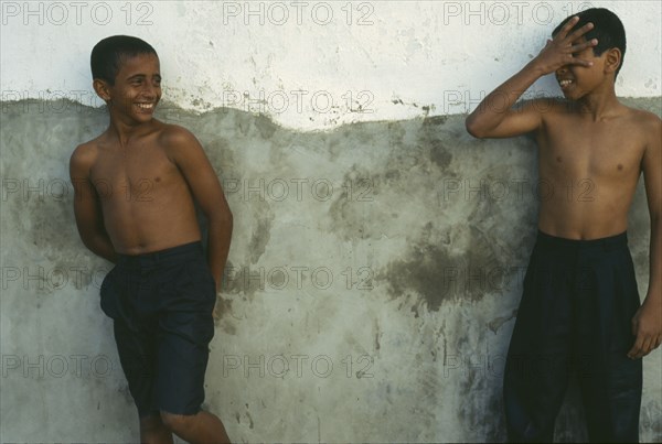 TANZANIA, Zanzibar Island, Zanzibar, Two wet boys wearing jeans leaning against wall and laughing to each other