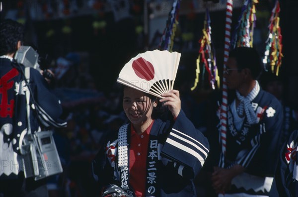 JAPAN, Honshu, Miyajima, Woman at the autumn Sake Festival holding a fan with the design of the Japanese flag on it