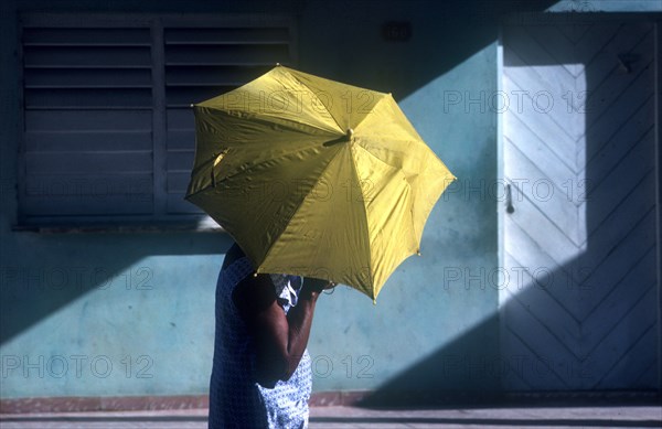 CUBA, Ciego De Avilar , Woman with yellow umbrella as sun shade in the street