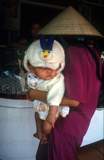 VIETNAM, Tay Ninh, Woman in a straw hat holding a baby as she looks at a shop display in Tay Ninh market.
