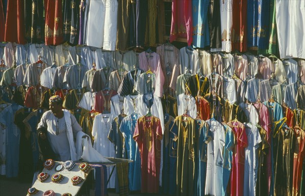 EGYPT, Luxor, Clothes stall in market with male vendor standing infront of racks hung with galabeyas.