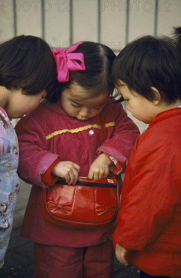 CHINA, Sichuan Province, Chengdu , Three young Chinese children looking in handbag wearing red and pink.