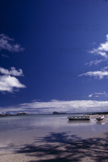 MAURITIUS,  , Grande Gaube, Sandy Beach with moored Boats and an Island in the distance with blue sky and whispy clouds above