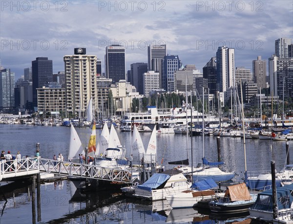 CANADA, British Columbia, Vancouver, City skyline over busy yacht harbour with people walking on the jetty