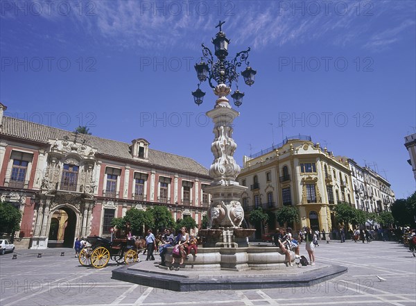 SPAIN, Andalucia, Seville, "Santa Cruz District, Plaza Virgen de los Reyes with Palacio Arzobispal on the left and a horse carriage passing a fountain with people sitting down"