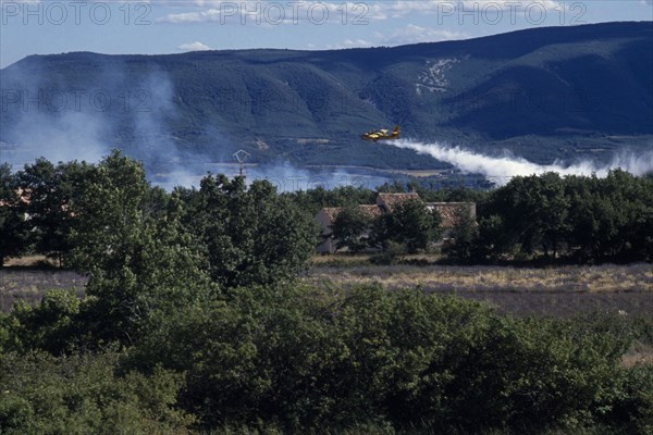 FRANCE, Provence Cote d’Azur, Luberon , Firefighter Plane flying towards smoke from a forest fire rising above green landscape.