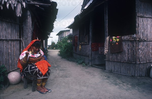 PANAMA,  , San Blas Islands, Cuna Indian woman sitting outside huts working on embroidery