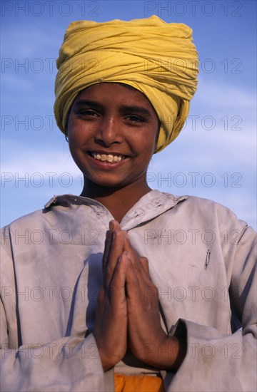 INDIA, Punjab, Amritsar , Portrait of smiling Sikh boy wearing yellow turban making gesture of greeting or namaste with his hands.
